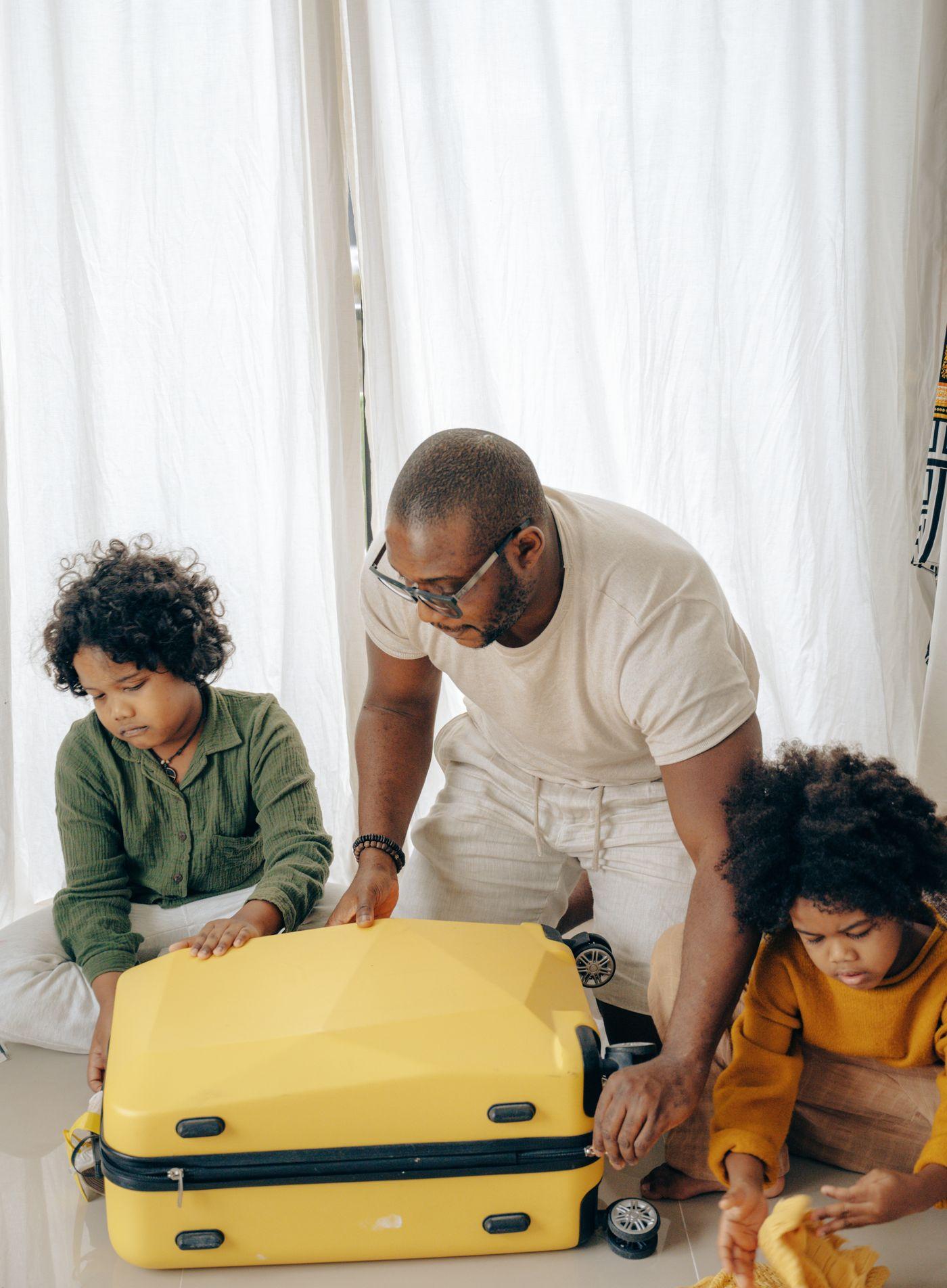 Un père et ses enfants préparent une valise jaune